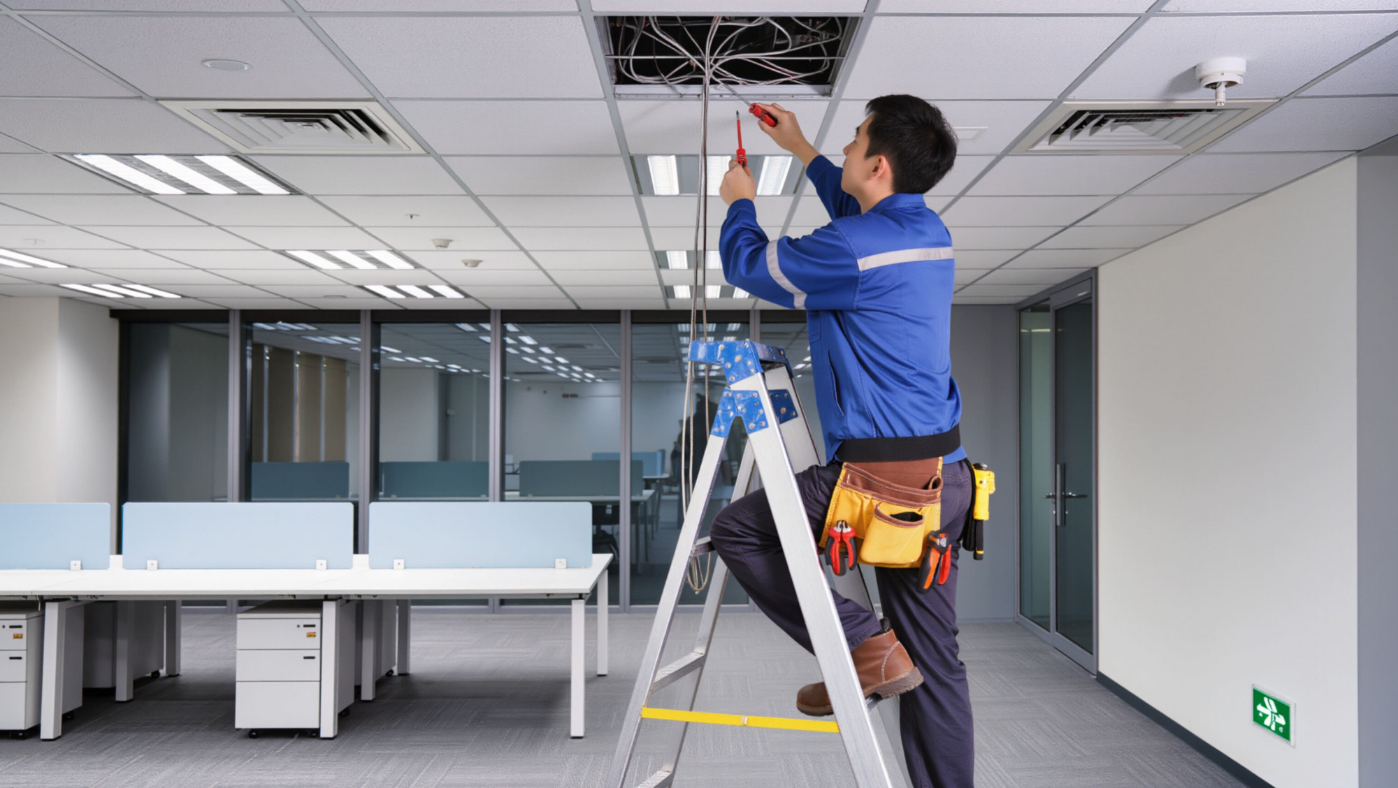 オフィスの天井で照明器具の取付作業を行う自社スタッフ
