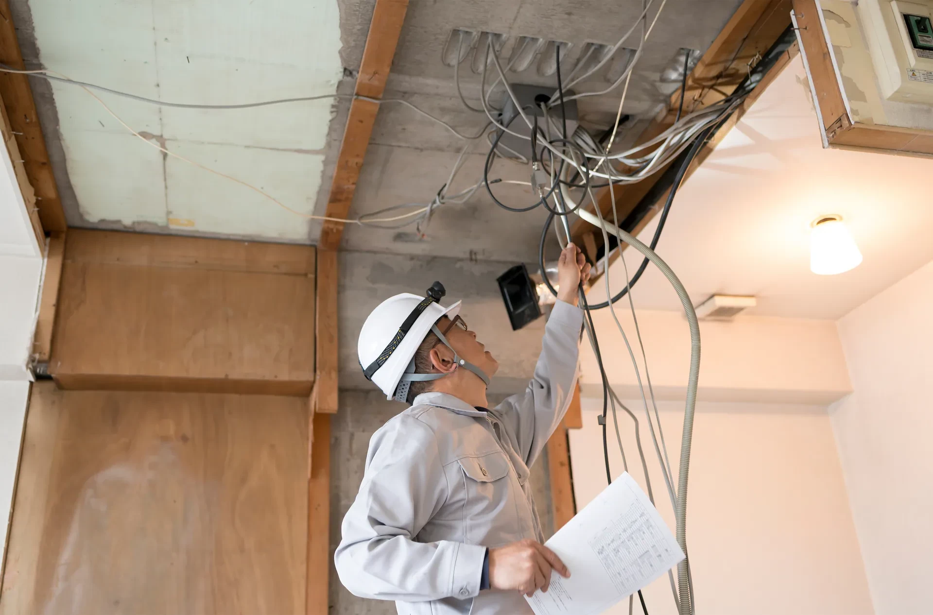 図面を手に天井裏の配線を確認する電気工事士