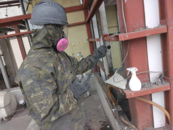 防護具を装備し、チッパーを使い石綿除去中