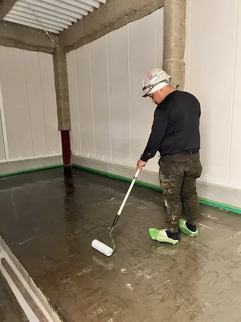 長柄の道具で塗床材を伸ばす職人