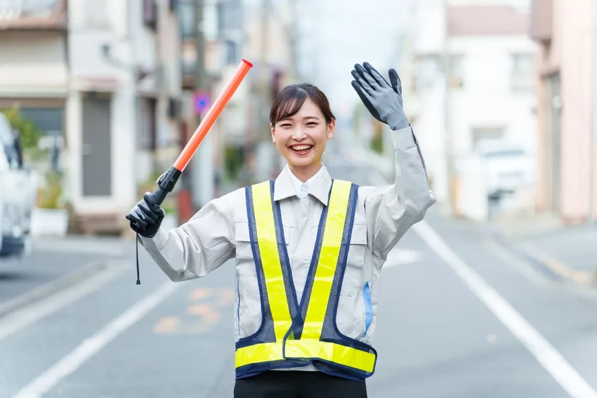 誘導棒を持ち笑顔で立つ女性警備員