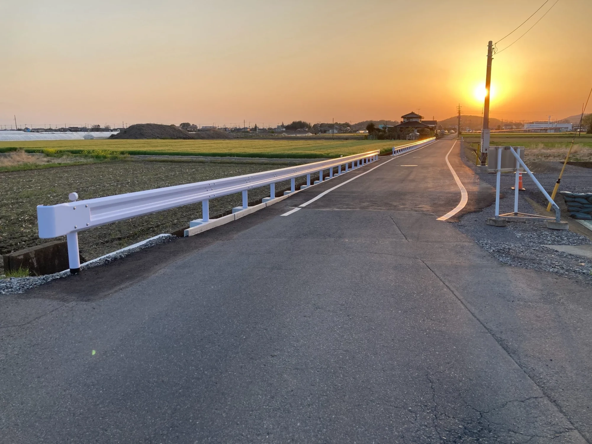 白いガードレールを設置し舗装を仕上げた田園の道路