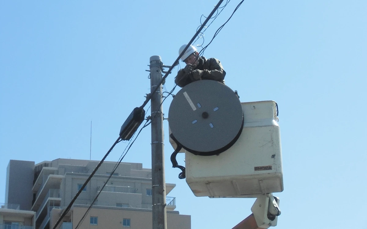 電柱上で２名が協力して通信設備の工事を行う様子