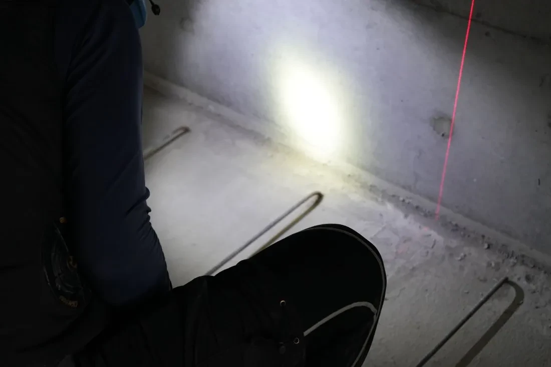 現場でしゃがみ、赤いレーザー基準線に合わせて作業するスタッフの足元